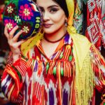 a woman wearing yellow scarf on her head holding a colorful round bag while looking at the camera
