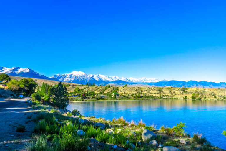 Shimmering turquoise alpine waters of Lake Issyk-Kul surrounded by the snow-capped Tian Shan mountain range in Kyrgyzstan.