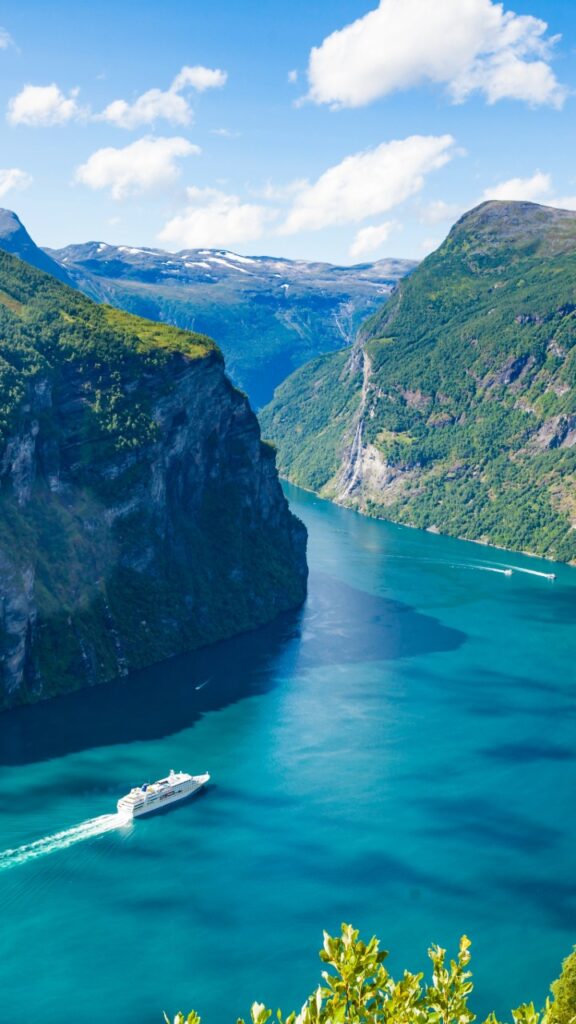 A cruise ship sailing through Geirangerfjord surrounded by steep cliffs and waterfalls in western Norway.