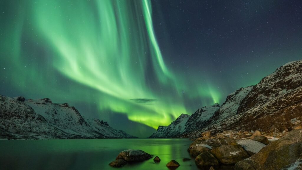 The Northern Lights glowing above snowy mountains and the city of Tromsø in Arctic Norway.