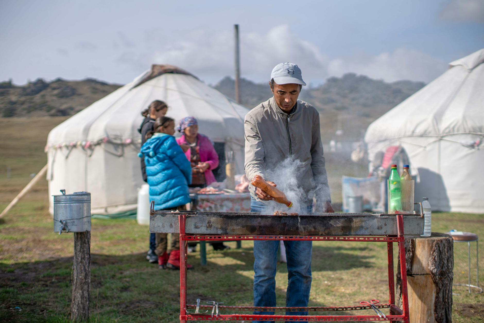 A man preparing traditional Central Asian cuisine outside a nomadic yurt village.