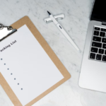 A packing list clipboard with a laptop and pen on a marble desk