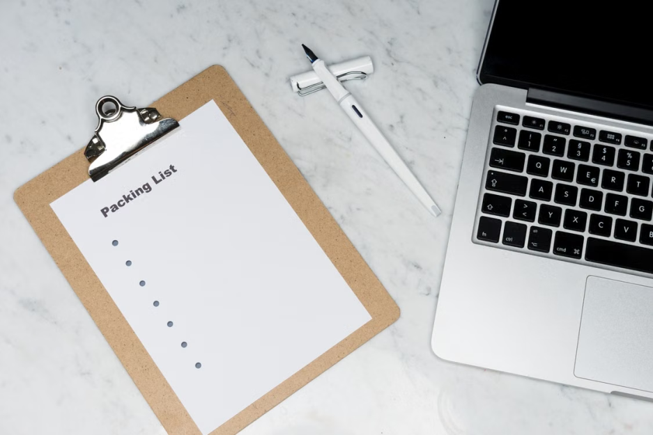 A packing list clipboard with a laptop and pen on a marble desk