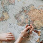 A person's hands planning a trip with a map, camera, and travel items