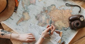 A person's hands planning a trip with a map, camera, and travel items