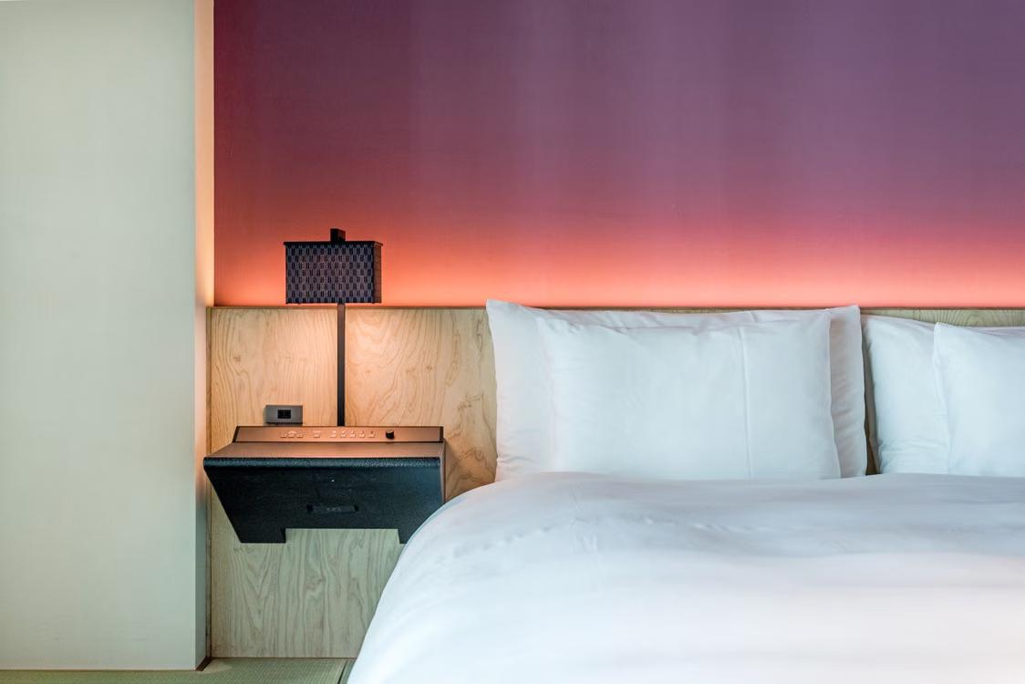 A modern, minimalist hotel room with elegant lighting and comfortable bed linen