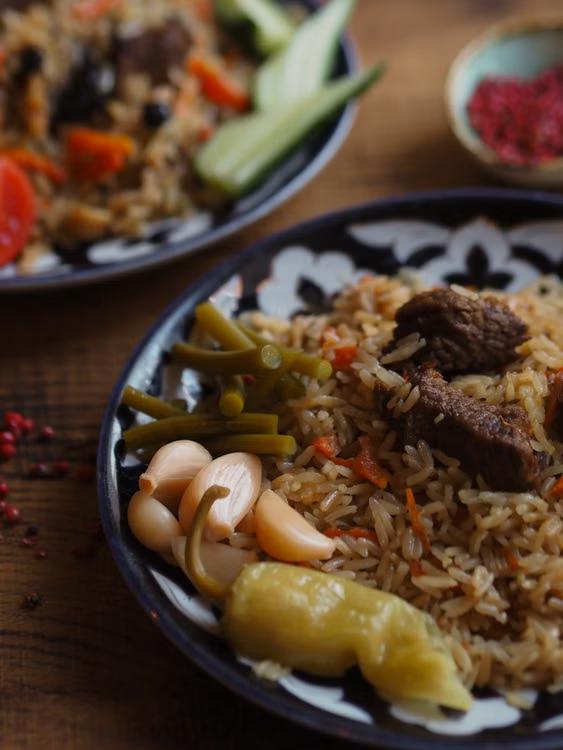 Close-up of a plov dish featuring rice, vegetables, and meat on a decorative plate