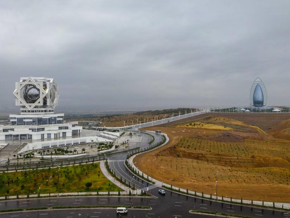 Modern white buildings and landscaped roads in Ashgabat, Turkmenistan, with mountains in the distance.