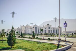 White marble building with landscaped grounds and mountain scenery in Ashgabat, Turkmenistan.
