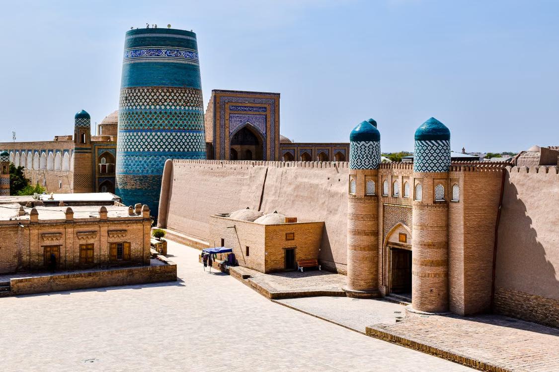 Historic brick buildings and turquoise domes surrounding a courtyard in Khiva, Uzbekistan.