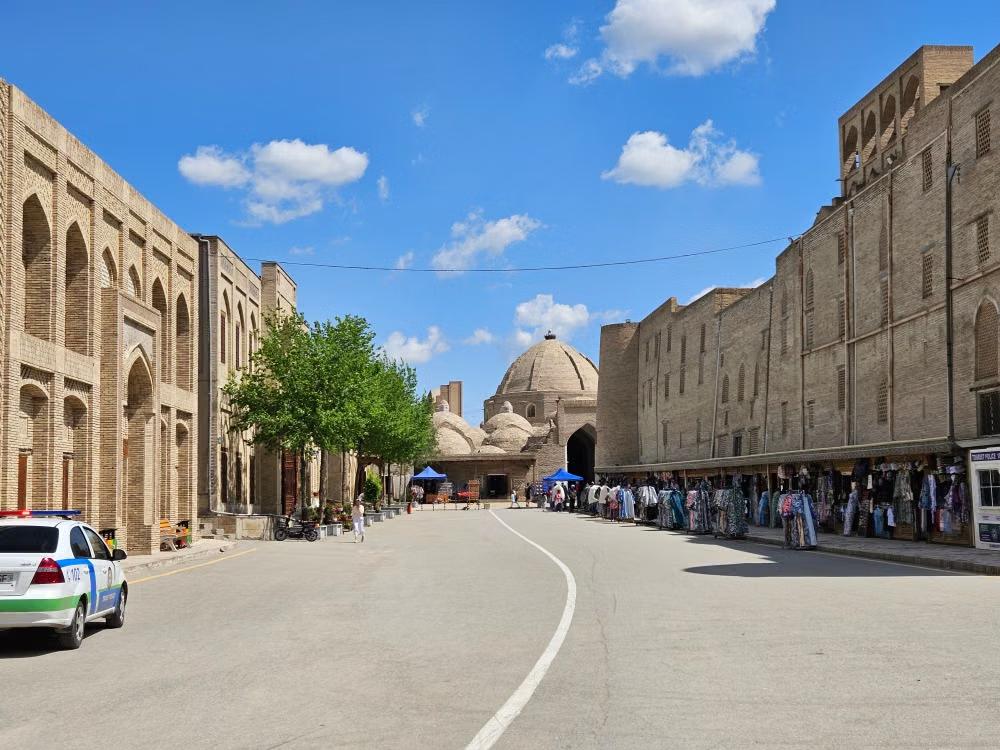 Historic brick buildings, arched facades, and market stalls along a street in Bukhara, Uzbekistan.