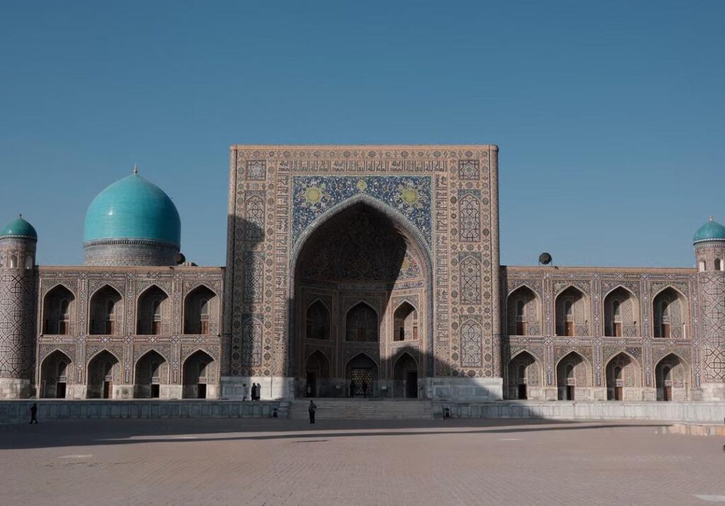 Ornate Islamic architecture with turquoise domes and a large tiled entrance at Registan Square in Samarkand, Uzbekistan.