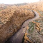 Rugged canyon landscape with a winding dirt road and a vehicle in Central Asia.