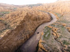 Rugged canyon landscape with a winding dirt road and a vehicle in Central Asia.