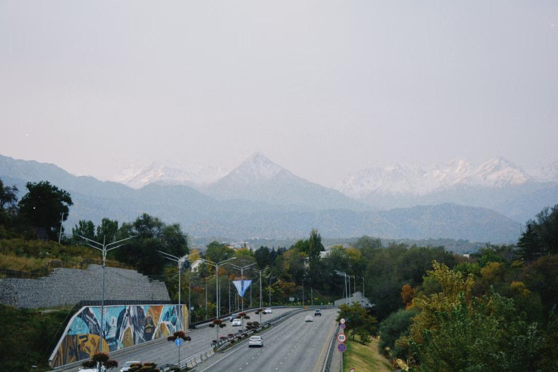 Scenic roadway with cars, autumn trees, and snow-capped mountains in Almaty, Kazakhstan.